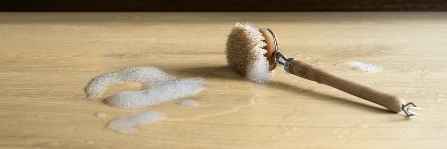 une brosse de nettoyage mouillée sur un sol stratifié Pergo beige